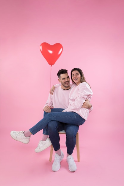 Free photo cheerful couple with heart balloon hugging on chair