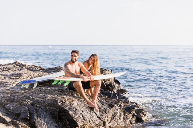 Cheerful couple with surfboards on rocky shore