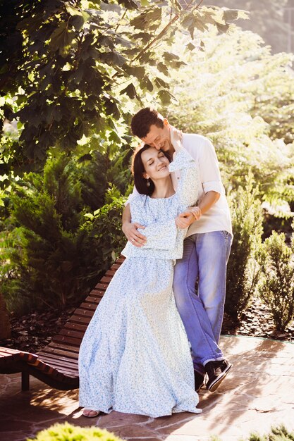 Cheerful curly man leans to his lady tender while she hugs him on wooden bench 