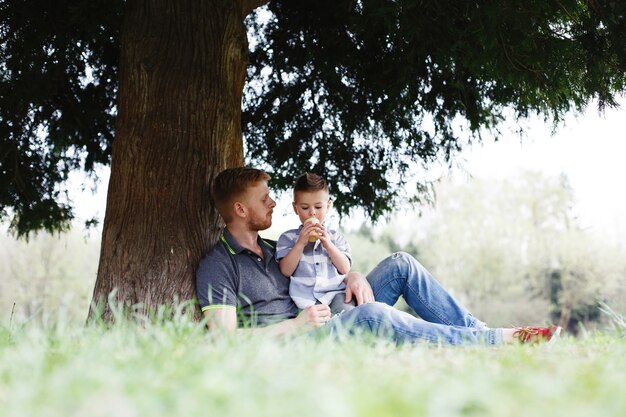 Cheerful dad and son have fun playing under the tree in park