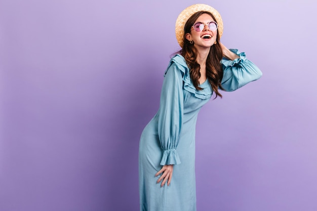 Free Photo cheerful darkhaired girl in great mood posing on isolated lilac background woman in stylish sky blue outfit and hat laughs