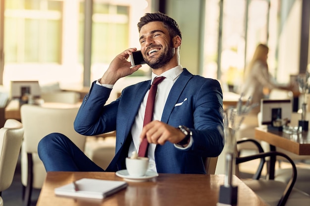 Cheerful entrepreneur making a phone call while having cup of coffee in a cafe