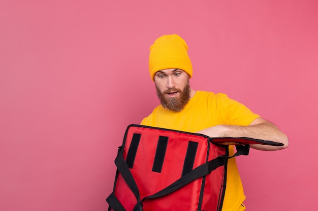 Free photo cheerful european bearded delivery man surprised emotions open box with food on pink