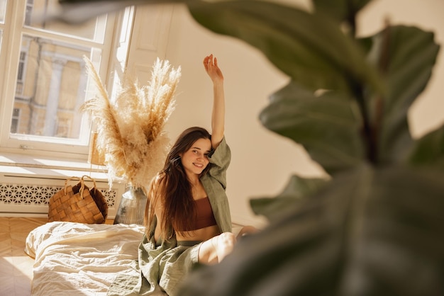 Free Photo cheerful fairskinned young girl smiling looking at camera while sitting on floor in comfortable room brunette woman with long hair wears casual clothes concept of rest and recovery