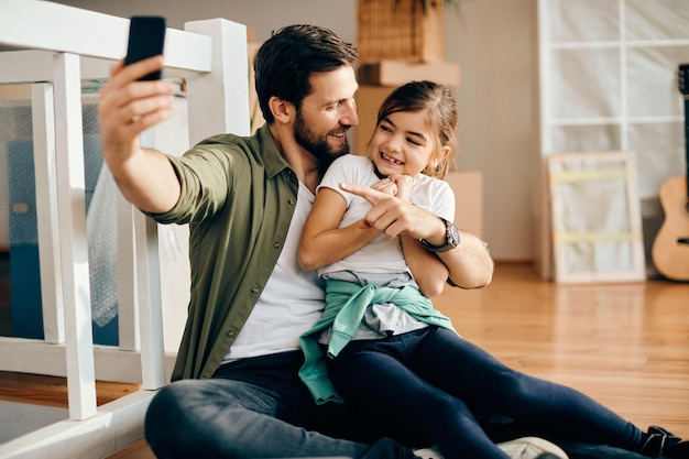 Free photo cheerful father and daughter having video call over smart phone at their new home