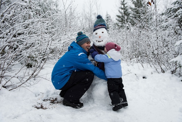 Cheerful father and daughter making snowman