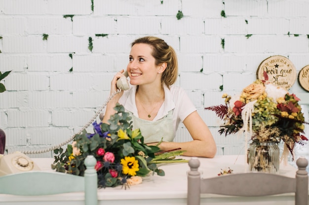 Cheerful florist speaking on phone at table