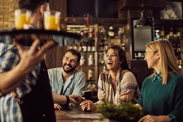 Cheerful friends having fun while talking to a waiter in a cafe