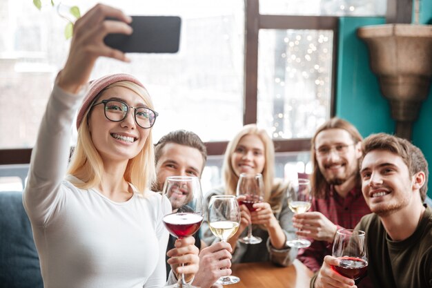 Cheerful friends sitting in cafe and make selfie by phone.