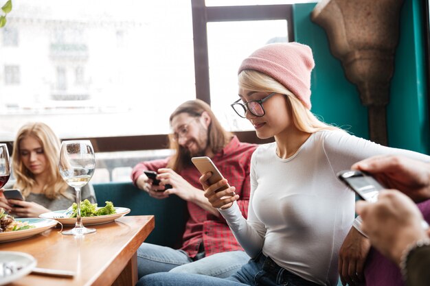 Cheerful friends sitting in cafe using mobile phones.