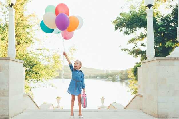 Cheerful girl holding colorful balloons and childish suitcase