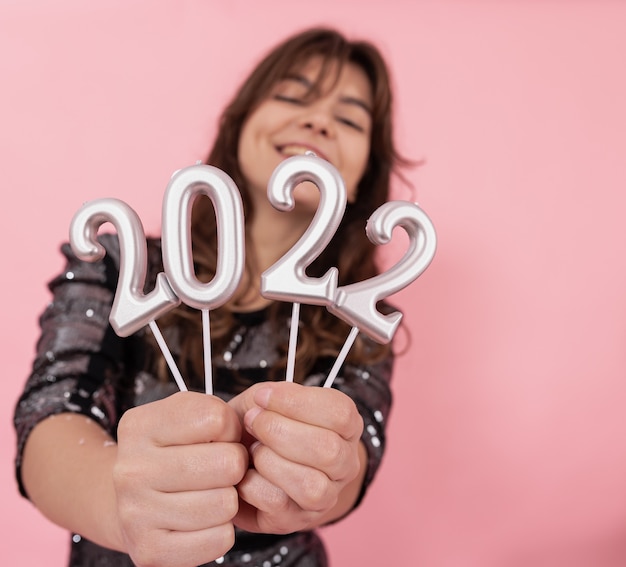 Cheerful girl on a pink background smiles and holds the numbers 2022 in her hands, celebrating the new year.