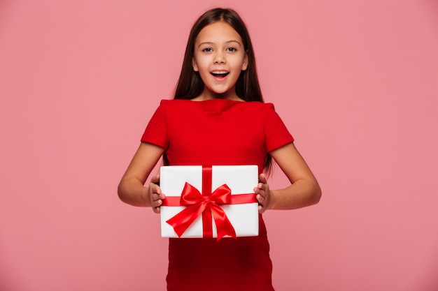 Cheerful girl showing gift and smiling isolated over pink