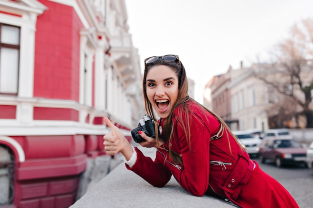 Cheerful girl in sunglasses expressing surprised emotions while walking around town with camera