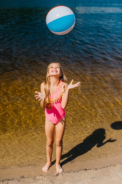 Cheerful girl throwing beach ball standing against sea