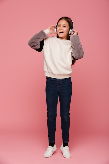 Cheerful girl using headphones and listening music isolated