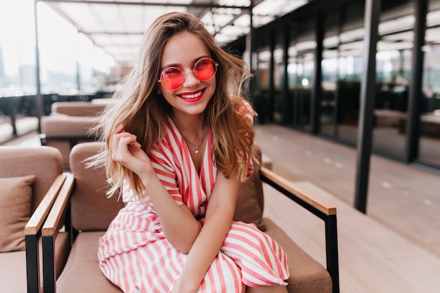 Free photo cheerful good-looking woman sitting in cafe with smile. indoor portrait of excited girl chilling on cozy chair.