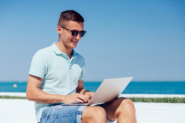 Cheerful guy in sunglasses working on laptop, typing, browsing websites