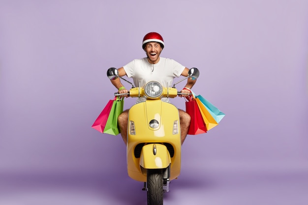 Free Photo cheerful guy with helmet and shopping bags driving yellow scooter