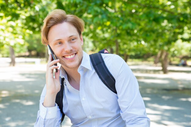 Cheerful happy student with backpack chatting on phone