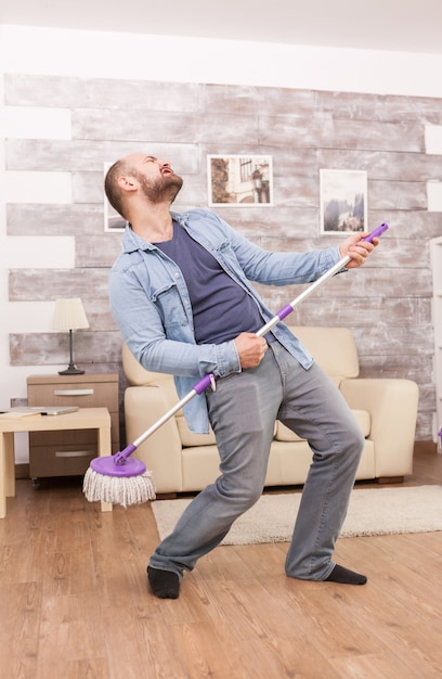 Cheerful husband dancing and cleaning the floor apartment