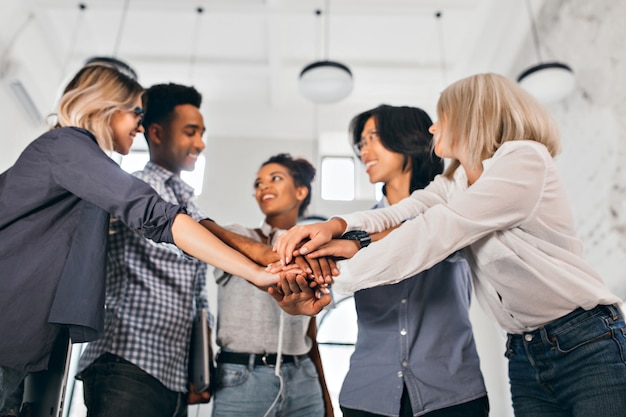 Free photo cheerful international students with happy face expression going to work together on science project. indoor photo of blonde woman in trendy blouse holding hands with coworkers.