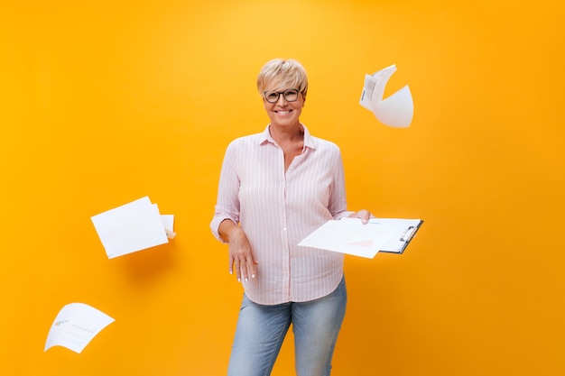 Free photo cheerful lady in eyeglasses, shirt and jeans poses with paper sheets