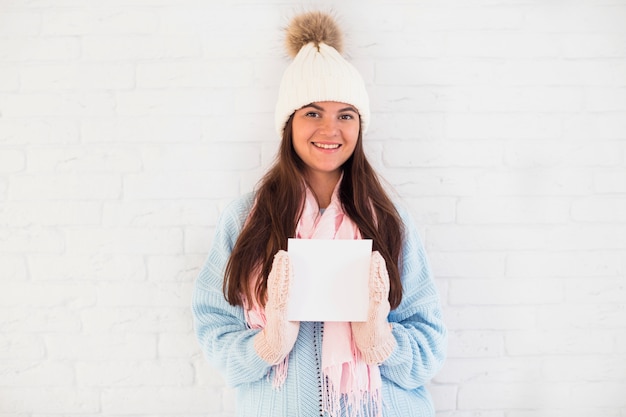 Free Photo cheerful lady in mittens, bobble hat and scarf with square paper 