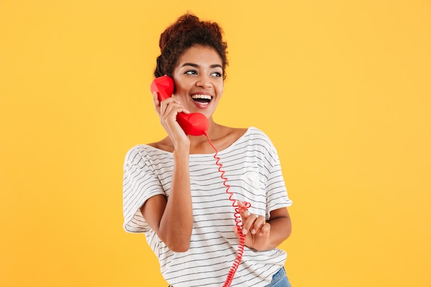 Cheerful lady talking on red telephone and looking aside