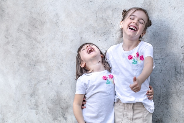 Free photo cheerful little girls on gray textured background. outdoor portrait little girl. gray textured wall background.