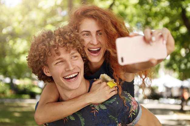 Free photo cheerful male and female resting outdoors taking selfies