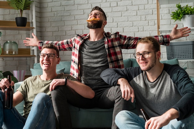 Cheerful male friends having pizza and beer and watching sports on tv