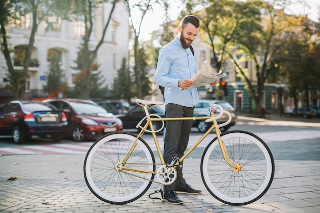 Free photo cheerful man reading newspaper near bike