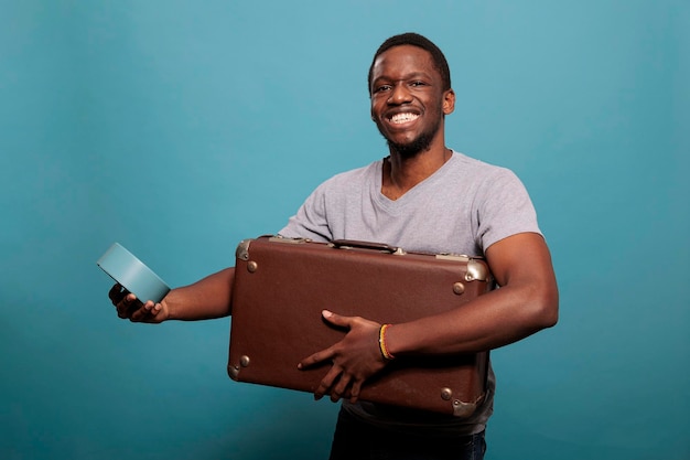 Cheerful man rushing with briefcase to leave for vacation, checking time on clock. Male model holding watch and suitcase bag to travel on urban voyage trip with journey luggage.