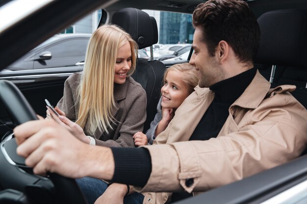 Cheerful man sitting in car with his wife and daughter