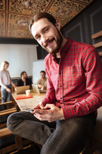 Cheerful man sitting in office and using phone