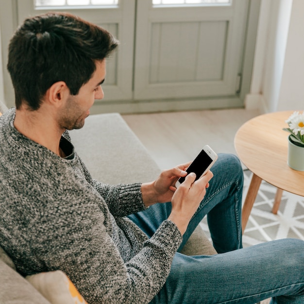 Free Photo cheerful man using smartphone on sofa