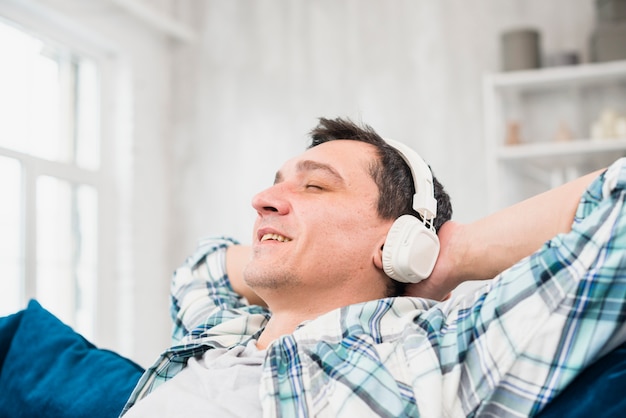 Free Photo cheerful man with closed eyes listening music in headphones on sofa