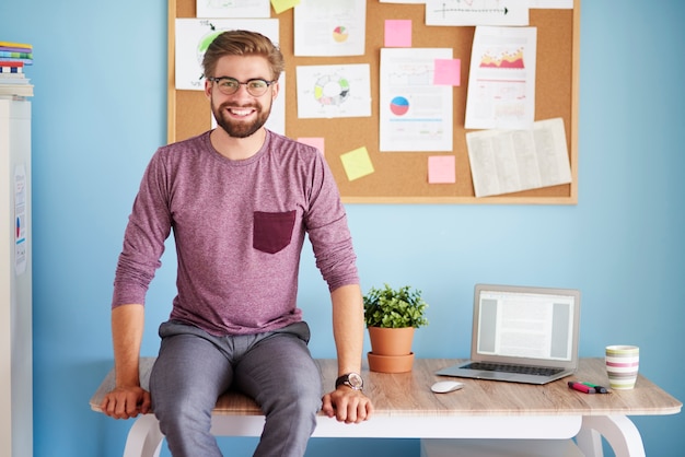 Free photo cheerful man witting on the office desk