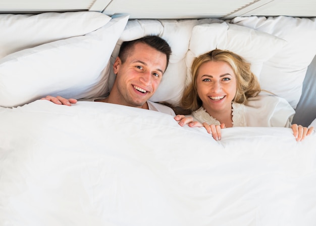 Cheerful man and young smiling woman under blanket 