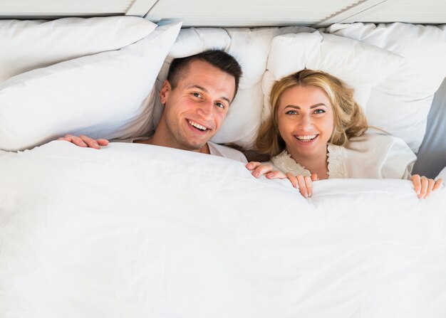 Cheerful man and young smiling woman under blanket 