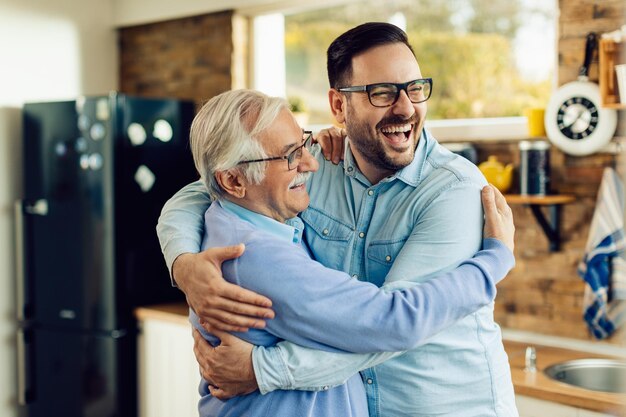 Cheerful mature man and his adult son embracing while greeting in the kitchen