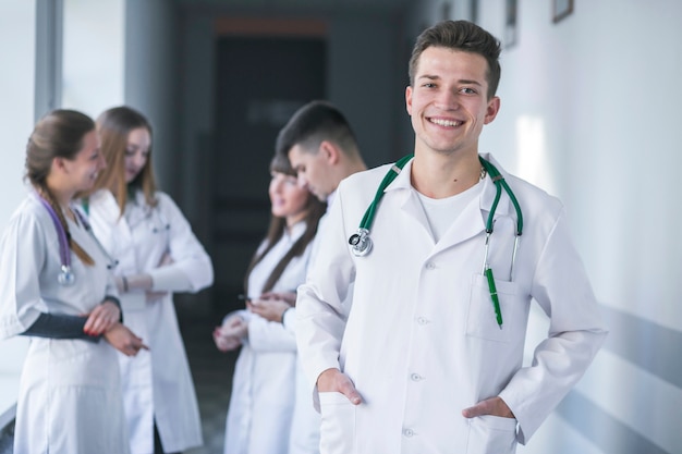 Cheerful medic standing with colleagues on background