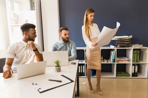 Free Photo cheerful men looking at woman with blueprint