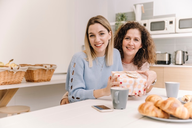 Cheerful mother and daughter with gift looking at camera