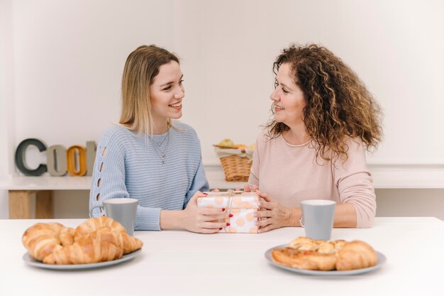 Cheerful mother and daughter with present during breakfast