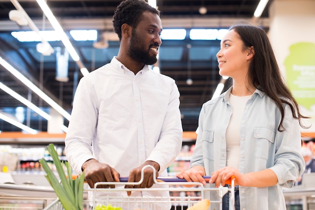 Cheerful multiethnic couple with shopping cart at supermarket  