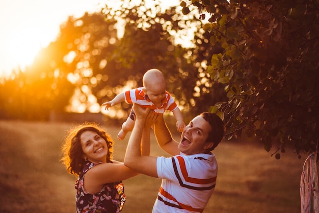 Cheerful parents hold their little son up standing outside in th