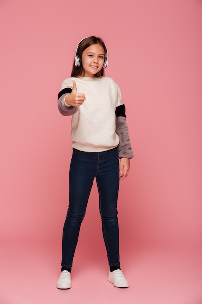 Cheerful positive girl in headphones showing thumb up isolated