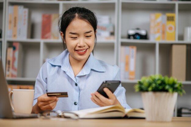 Cheerful pretty young woman using mobile phone shopping online and payment by credit bank card